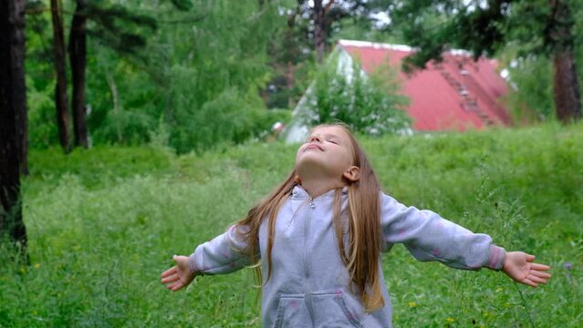 Child girl in the meadow with raised hands, deep breathing. Forest after rain with fresh air. Enjoying Life