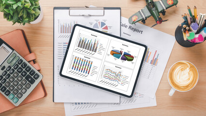 Fototapeta na wymiar Tablet with charts and reports, calculator, pen, eyeglass and coffee on wooden desk workplace. Top view flat lay with copy space.