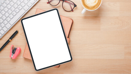 Wooden desk workplace with blank screen tablet, keyboard, notebook, eyeglass, pen and cup of coffee, Top view flat lay with copy space.