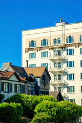 Fototapeta premium Row of modern houses in late afternoon shade with decorative rooftops front yard trees with urban commercial building
