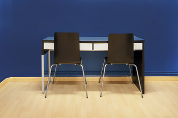 Obraz premium Study table attached to the simple blue black wall with metal legs and glass top with two black chairs