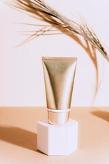 Golden cream tube on a podium with harsh shadow. Dry palm leaf on the background