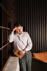 Portrait of a young serious man standing against a book with a book or notebook in his hand.