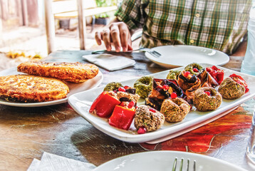 Rolls of eggplant with filling of walnuts and Georgian phali of spinach with berbs and pomegrante seeds and cheese-filled bread  on outside resturant table with male preparing to eat it--shallow focus