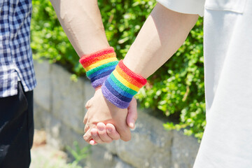 虹色のリストバンドをして手を繋ぐ男性カップルの手元