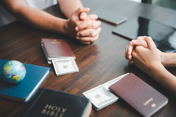 Concept of Christian ministry. Small groups pray together for Christian mission. Mission to spread gospel and religion of Christianity. Hands praying with dollar and passport on wooden table.