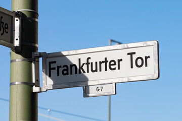Fototapeta premium Frankfurter Tor road name sign in Berlin Friedrichshain. Metal frame with a white plate inside. The letters are printed in black on the plate. Location name at an intersection.