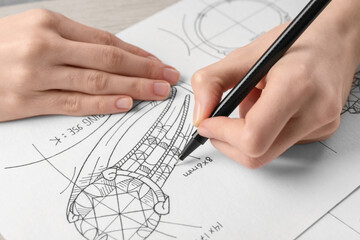 Jeweler drawing sketch of elegant ring on paper at wooden table, closeup