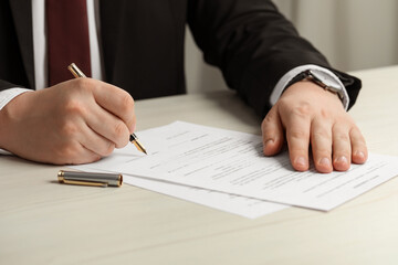 Notary signing document at wooden table, closeup