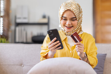 Easy payments. Smiling arabic woman or muslim woman in hijab in headscarf using phone and credit card at home, paying for utilities online, free space