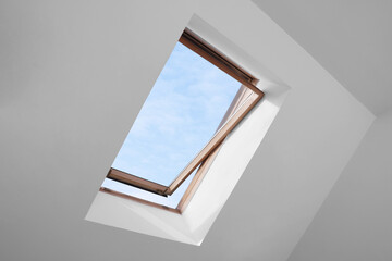 Open skylight roof window and lamps on slanted ceiling in attic room, low angle view