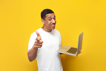 I choose you. young african american guy in white t-shirt uses laptop and points at you on yellow background