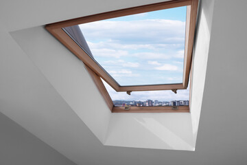 Open skylight roof window on slanted ceiling in attic room