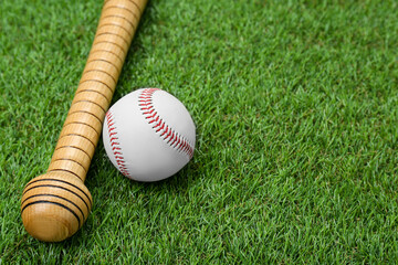 Obraz na płótnie Canvas Wooden baseball bat and ball on green grass, closeup. Space for text