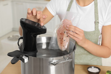 Woman putting vacuum packed meat into pot and using thermal immersion circulator, closeup. Sous...