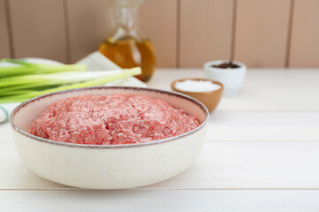 Bowl of raw fresh minced meat on white wooden table, closeup. Sp