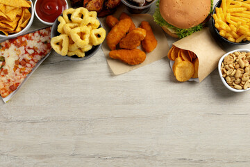 French fries, chicken nuggets and other fast food on white wooden table, flat lay with space for text