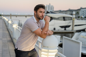 Fototapeta premium Rich business man dreaming and thinking near the yacht. Handsome man outdoors portrait. Portrait of stylish male model outdoor. Fashionable man in urban style.