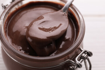 Jar with tasty chocolate paste and spoon on white wooden table, closeup