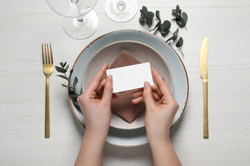 Woman holding adjusting stylish table setting with eucalyptus leaves and cutlery on white wooden background, closeup