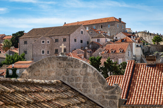 Photo of stone buildings with red tile roofs and a cross along the top of the walls of the old town of Dubrovnik, Croatia, a remarkably well-preserved UNESCO site.