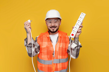 asian electrician in uniform holds extension cord and connects electricity on yellow isolated background