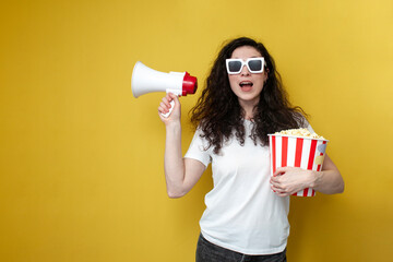 young curly girl spectator in white t-shirt and 3d glasses holds large bucket of popcorn and...