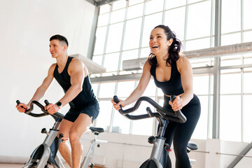 athletic couple of cyclists train on static bicycle simulator, man trainer and fitness woman go in for sports together
