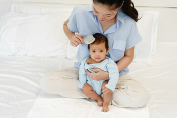 Obraz na płótnie Canvas mother combing her newborn baby hair on bed