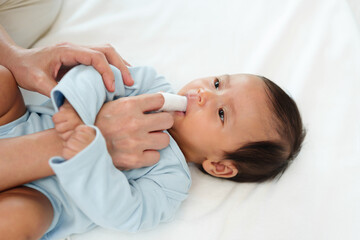 mother using finger to clean newborn baby mouth (tongue and gum) with clean gauze on bed - obrazy, fototapety, plakaty