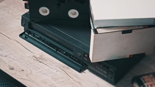 Insert VHS cassette into VCR player. Black vintage videotape cassette recorder on a desk with many archived video cassettes. Male hand inserting old VHS Tape into a retro player. Home video, nostalgia