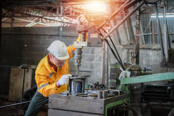 Engineer wearing yellow work clothes white hardhat and wear glove working with drilling machine, Industry and production concept.