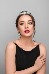 Beautiful young woman wearing luxurious tiara on light grey background