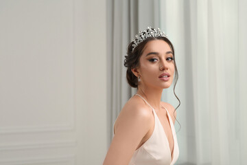 Beautiful young woman wearing luxurious tiara indoors, space for text