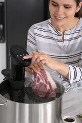 Woman putting vacuum packed meat into pot and using thermal immersion circulator. Sous vide cooking