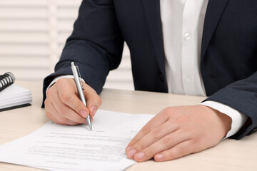 Man signing document at wooden table, closeup