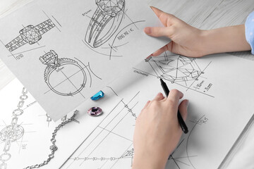 Jeweler with sketches of elegant jewelry at white wooden table, closeup