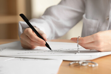 Jeweler drawing sketch of elegant bracelet on paper at wooden table indoors, closeup