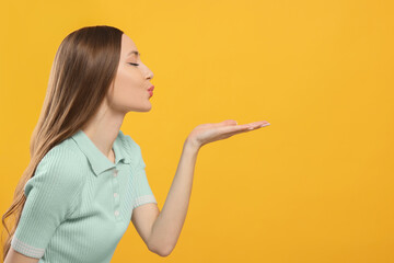 Beautiful young woman blowing kiss on yellow background, space for text - obrazy, fototapety, plakaty