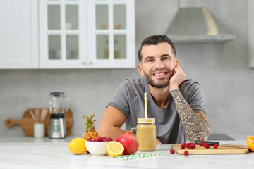 Fototapeta na wymiar Handsome man with delicious smoothie and ingredients at white table in kitchen. Space for text