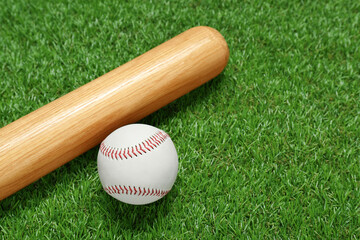 Obraz na płótnie Canvas Wooden baseball bat and ball on green grass, closeup. Sports equipment