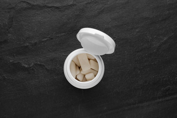 Jar with chewing gums on black table, top view