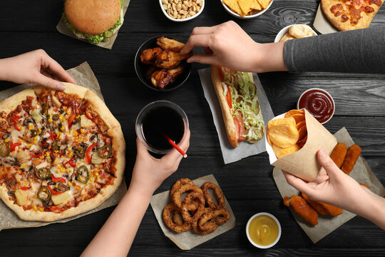 Friends Eating Pizza, Chicken Wings And Other Fast Food At Black Wooden Table, Top View