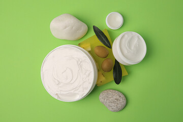 Different cosmetic products with olives and stones on light green background, flat lay