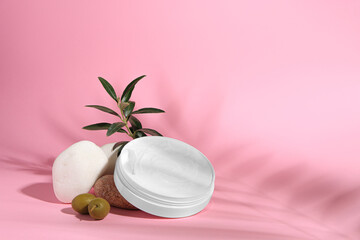 Jar of natural cream, stones and olives on pink background, space for text. Cosmetic products