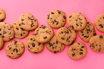 Many delicious chocolate chip cookies on pink background, flat lay