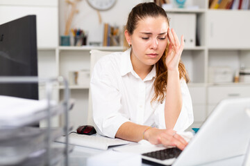 Tired young woman secretary sitting alone near laptop computer and upset after receiving mail