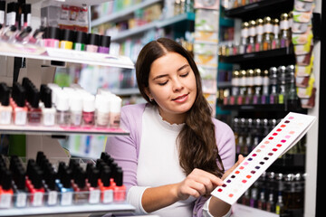 Young girl choosing nail polish from color samples in makeup store