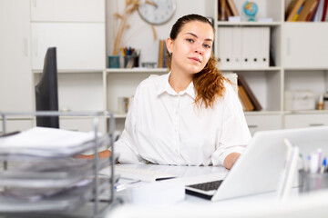 Focused young woman secretary working alone at her workplace on laptop