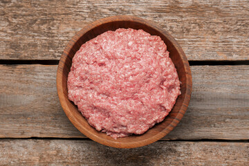 Bowl with raw fresh minced meat on wooden table, top view
